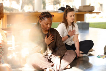 Deux femmes en méditation assises au sol - main sur le cœur - lumière dorée baignant la pièce - connexion à soi et cohérence cardiaque lors de la retraite Marrakech Les Rayonnantes